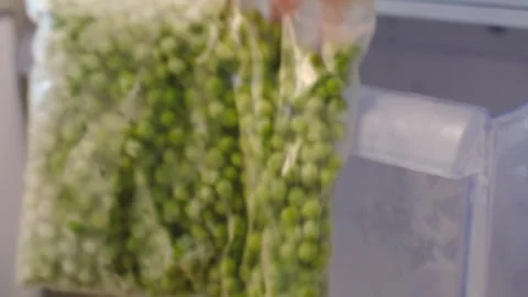 Female hand holding zip bag with frozen green peas against open freezer Stock Footage 304565409