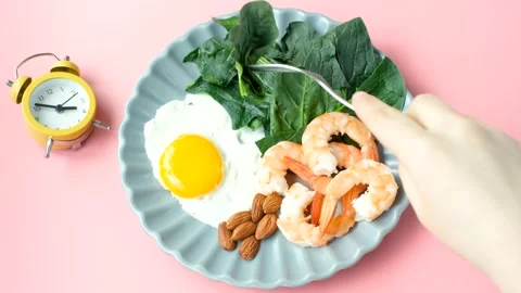 Female hand holds a fork next to plate of food and alarm clock, concept of a Stock Footage 236985662