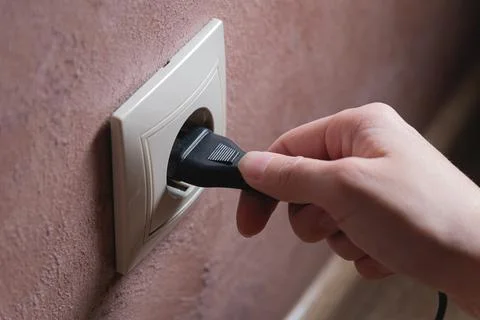 A female hand inserts an electric plug into a euro-format socket close-up Stock Photos