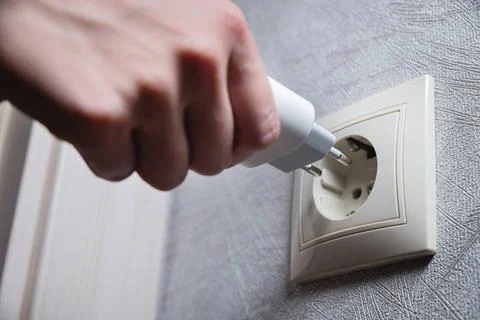 A female hand inserts an electric plug into a euro-format socket close-up ... Foto stock