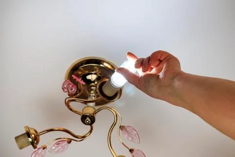 Female hand inserts a light bulb into the threaded socket. she is shining. In Stock Photos