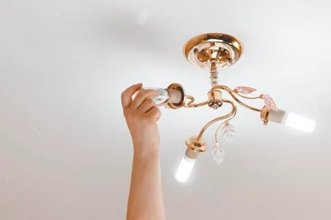 Female hand inserts a light bulb into the threaded socket. she is shining. In Stock Photos