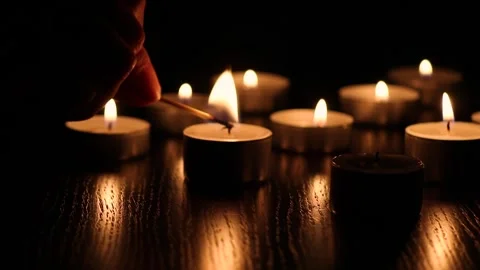 Female hand lighting candles on table in darkness, warm candlelight glow in Stock Footage 331140508