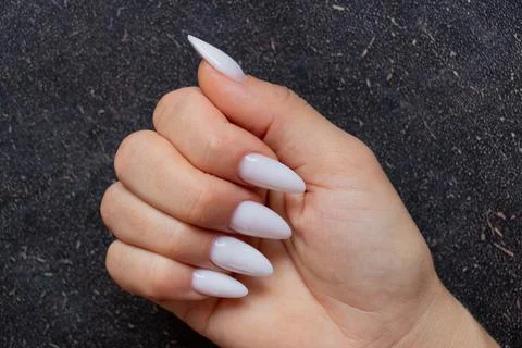 Female hand with long sharp white manicure on black background Stock Photos