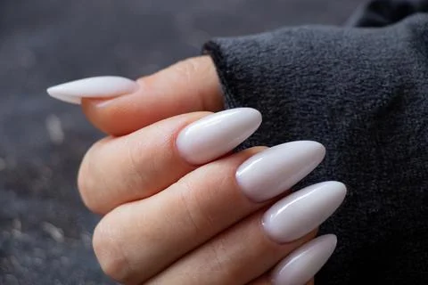 Female hand with long sharp white manicure on black background Stock Photos