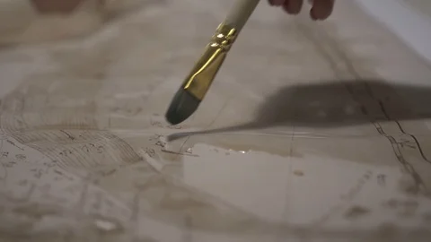 Female hand make aged map with paint brush and transparent watercolor, close-up Vidéo 94764822