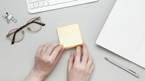 Female hand making reminder note on adhesive memo paper placed on tidy desk w Foto stock