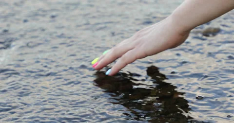 A female hand with a  multi-colored manicure pulls out a pebble from the river Stock Footage 135487226