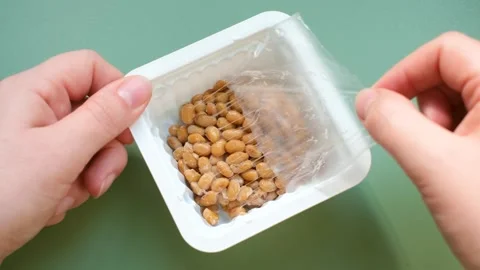 Female hand opens plastic box with japanese natto beans on green background. Stock Footage 291757595