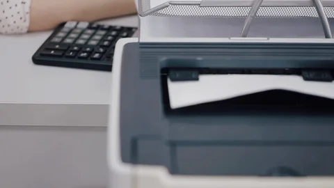 A female hand picks up a printed document from the printer. Vidéo 129384626