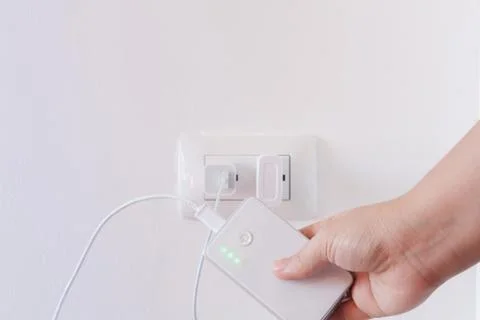 Female hand plugging in the plug of her power bank in a socket Foto stock