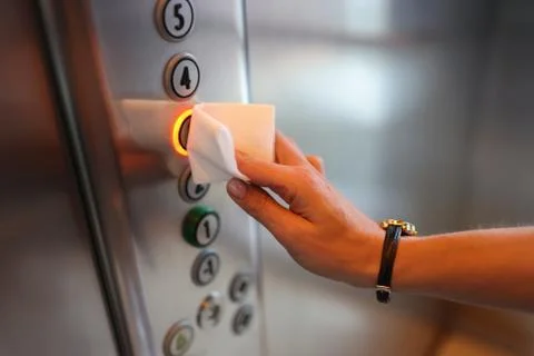 Female hand presses button in elevator through napkin. Stock Photos