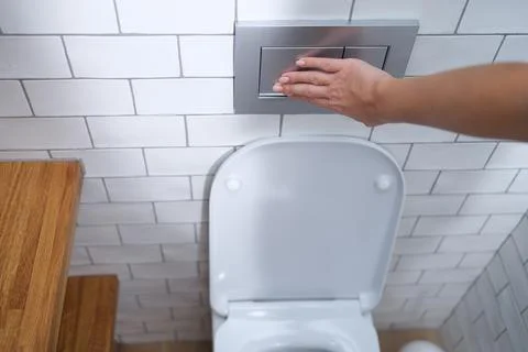 Female hand presses flush button in toilet closeup Photos