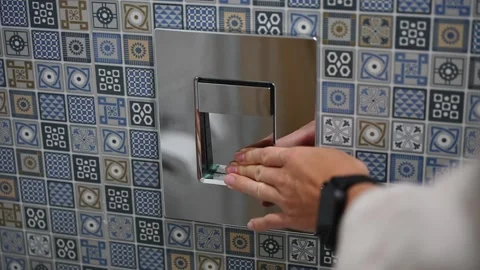 Female hand pressing chrome flush button on a wall with blue pattern tiles Stock Footage 333332691