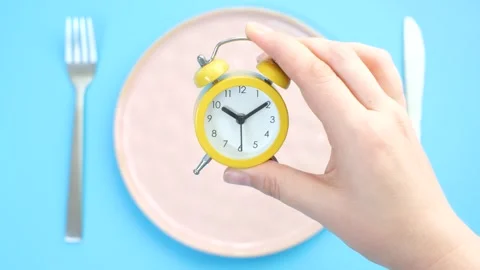 Female hand puts an alarm clock on an empty plate on blue background, top view. Stock Footage 288777948