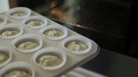 A female hand puts a baking tray with handmade muffin's dough inside a home oven Video stock 81473785