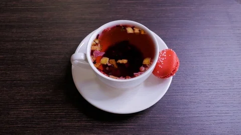 Female hand puts cup of tea with red macaroon on wooden table in cafe Stock Footage 106816688
