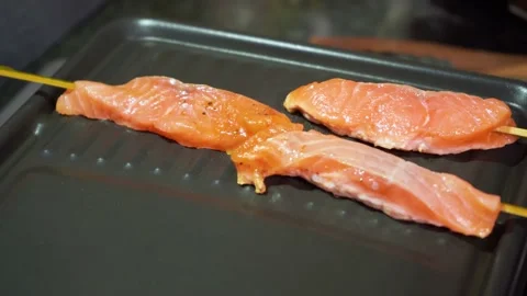 Female hand puts on pan raw salmon skewers with soy lime bbq sauce natural food Stock Footage 157112542