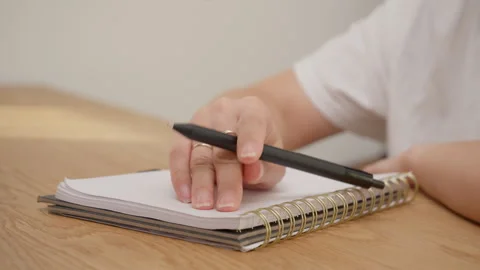 Female hand rhythmically tapping black pen on spiral notebook page with audio Stock Footage 327647600