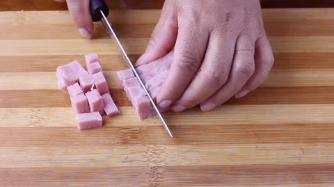 Female hand slicing raw ham cubes on cutting board Stock Footage 252478747