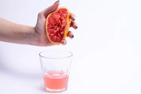 Female hand squeezes of a grapefruit, grapefruit juice on white background Stock Photos
