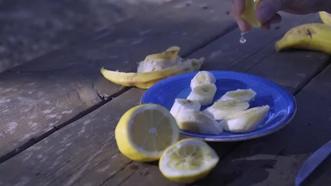 Female hand squeezing fresh lemon juice over sliced bananas on a blue plate. Stock Footage 342452503