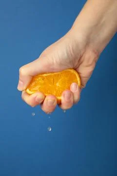 Female hand squeezing half of orange on blue background. Stock Photos