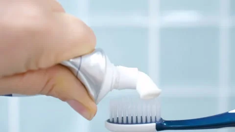 Female hand squeezing toothpaste onto toothbrush against blue tile background. Stock Footage 314753023