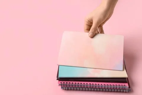 Female hand with stack of different notebooks on pink background Stock Photos