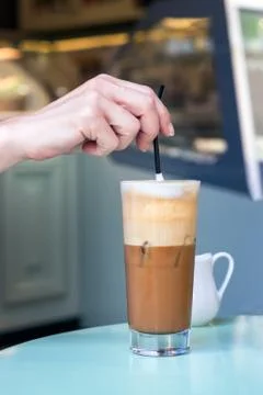 Female hand stirring a straw on a greek cold coffee, freddo cappuccino, outdoors Stock Photos