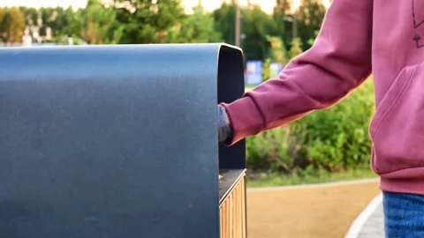 A female hand throwing a beer bottle into a trash bin in a park Video stock 313462487