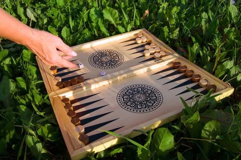 Female hand throwing a dice in a backgammon board game on a summer lawn in a  Stock Photos