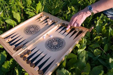 Female hand throwing a dice in a backgammon board game on a summer lawn in a  Stock Photos