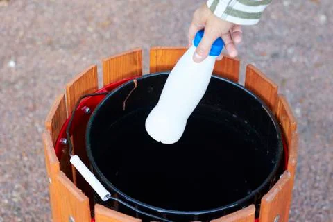Female hand throws an empty plastic bottle in a city street trash can, close- Stock Photos