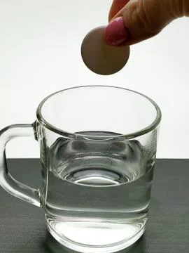 Female hand throws quick-dissolving tablet in a glass of water close-up Stock Photos