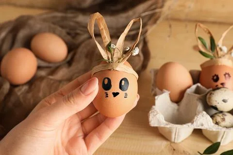Female hand with tray of creative Easter eggs, fabric and flowers on brown wo Stock Photos