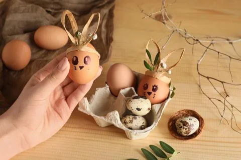 Female hand with tray of creative Easter eggs, fabric and flowers on brown wo Stock Photos