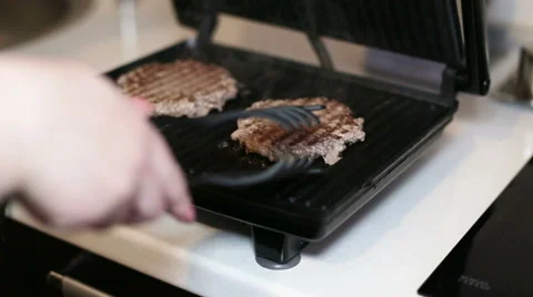 Female hand turns steak on electric grill . Close-up Vidéo 60572053