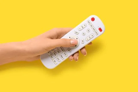 Female hand with TV remote controller on yellow background 库存照片