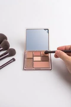 Female hand using brush on eyeshadow palette with mirror isolated on white .. Stock Photos