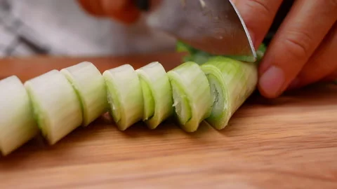 Female hand using kitchen knife to cut Japanese Scallion on wooden cutting board Stock Footage 157085291