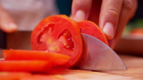 Female hand using kitchen knife to cut ripe tomato on wooden cutting board.  Vídeo Stock 157085324