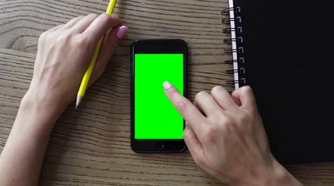 Female hand using smart mobile phone with a green screen on wooden table Stock Footage 67648493