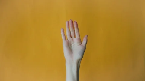 Female hand is waving while on an orange background. Hand gesture, goodbye Stock Footage 125620857
