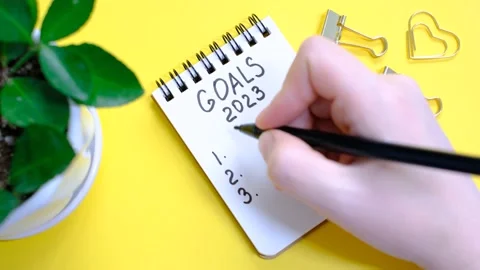 Female hand writes in a paper notebook goals 2023 close-up on yellow background. Stock Footage 228708279