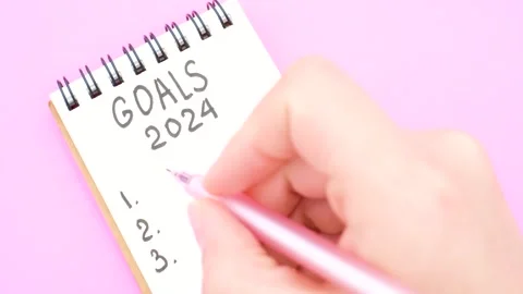 Female hand writes in a paper notebook goals 2024 close-up on a pink background. Video stock 250598922