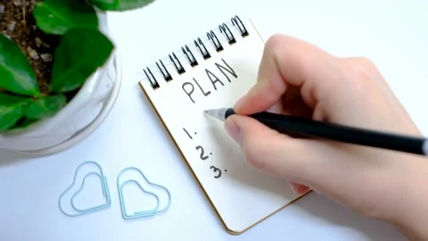 Female hand writes a plan in notebook on a white background top view. Stock Footage 228670612