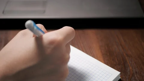Female hand writes something in notebook with pen, next to it is laptop. Close Vídeos de archivo 126064162