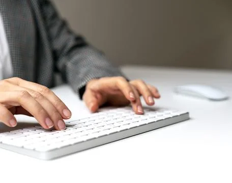 Female hands and wireless computer keyboard on white desk. Stock Photos