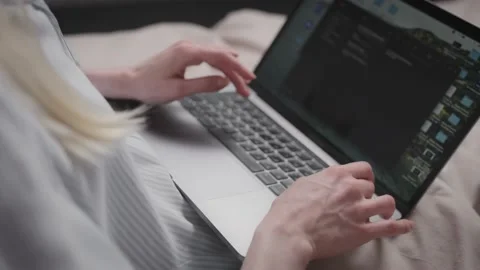 Female hands are typing on the laptop keyboard. Woman is lying in bed. Stock Footage